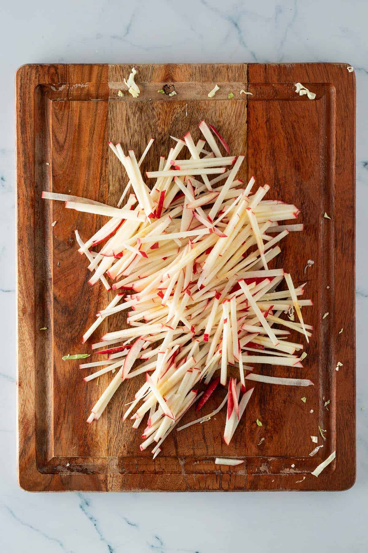 In d&uuml;nne, feine Stifte geschnittener Apfel auf einem Holzbrett.