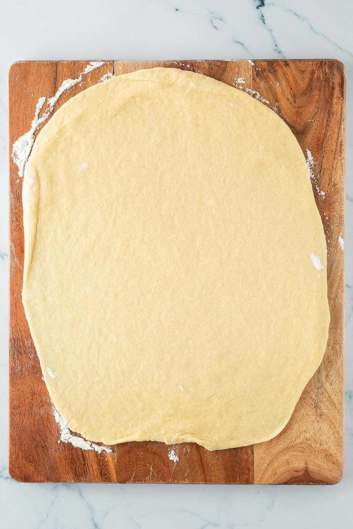 Dünn ausgerollter Hefeteig auf einem Holzbrett, bereit zum Bestreichen mit Füllung.