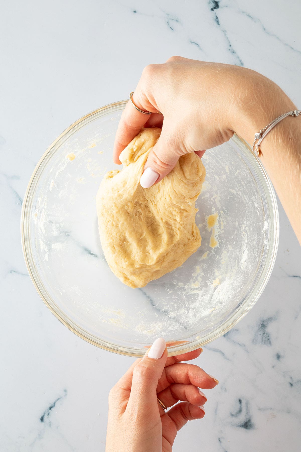 Hände dehnen den Hefeteig in einer Glasschüssel, um ihn geschmeidig zu machen.