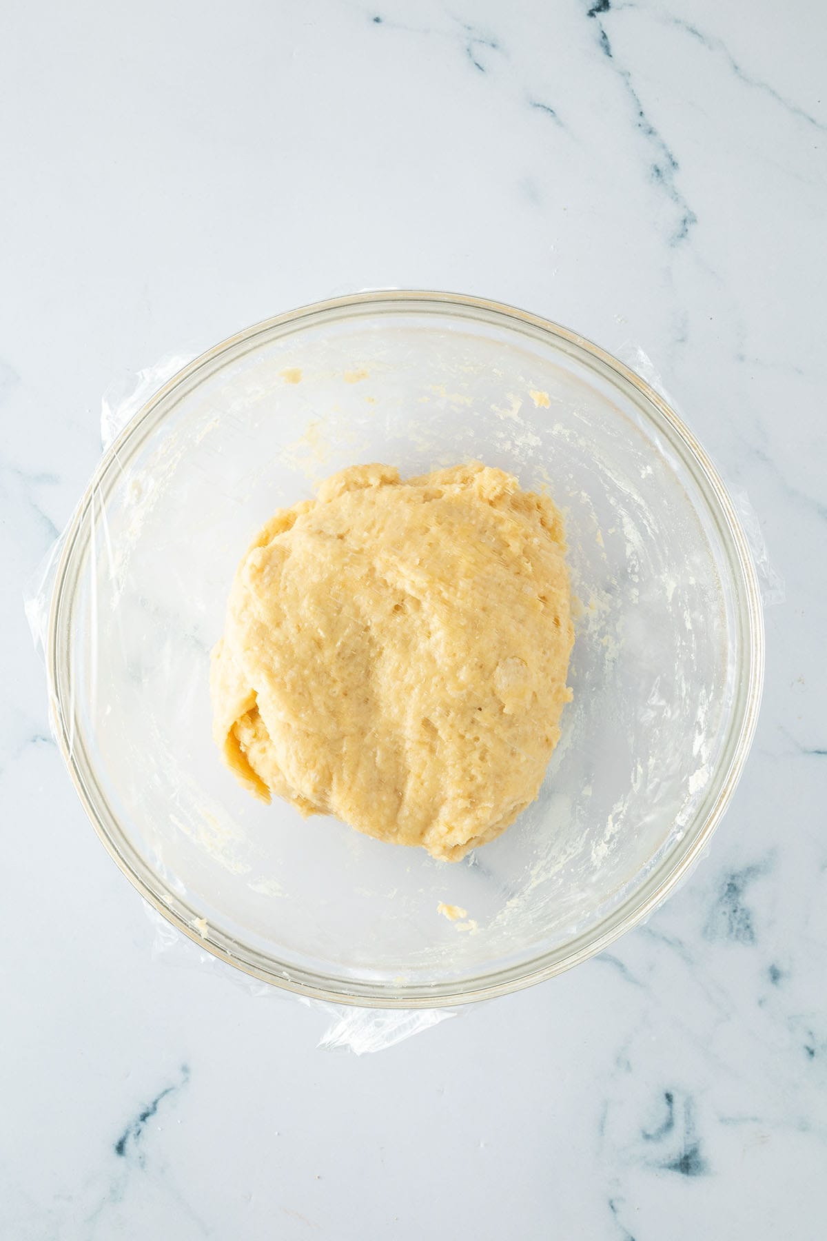 Hefeteig in einer Schüssel nach dem Verkneten, mit Folie abgedeckt.