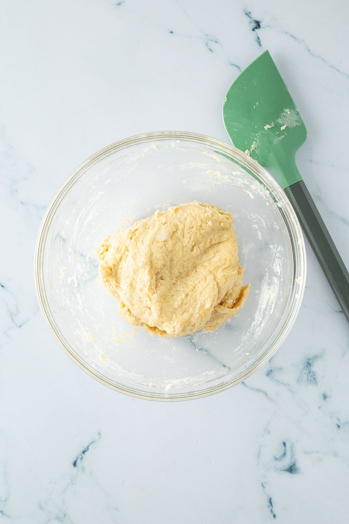 Weicher Hefeteig in einer Schüssel mit grünem Teigschaber daneben.