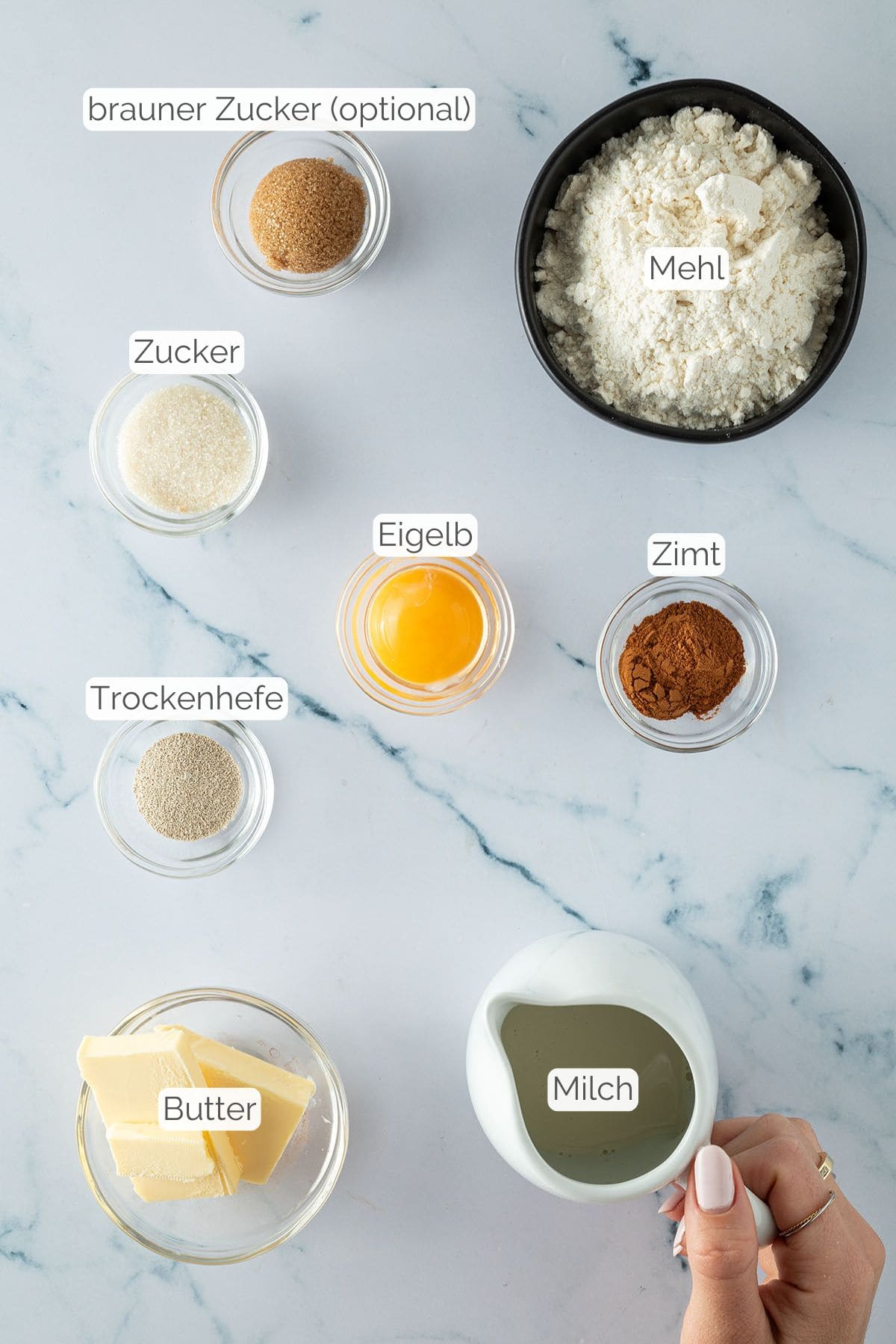 Alle Zutaten mit jeweiliger Textbeschriftung, die für eine kleine Portion Zimtschnecken benötigt werden.