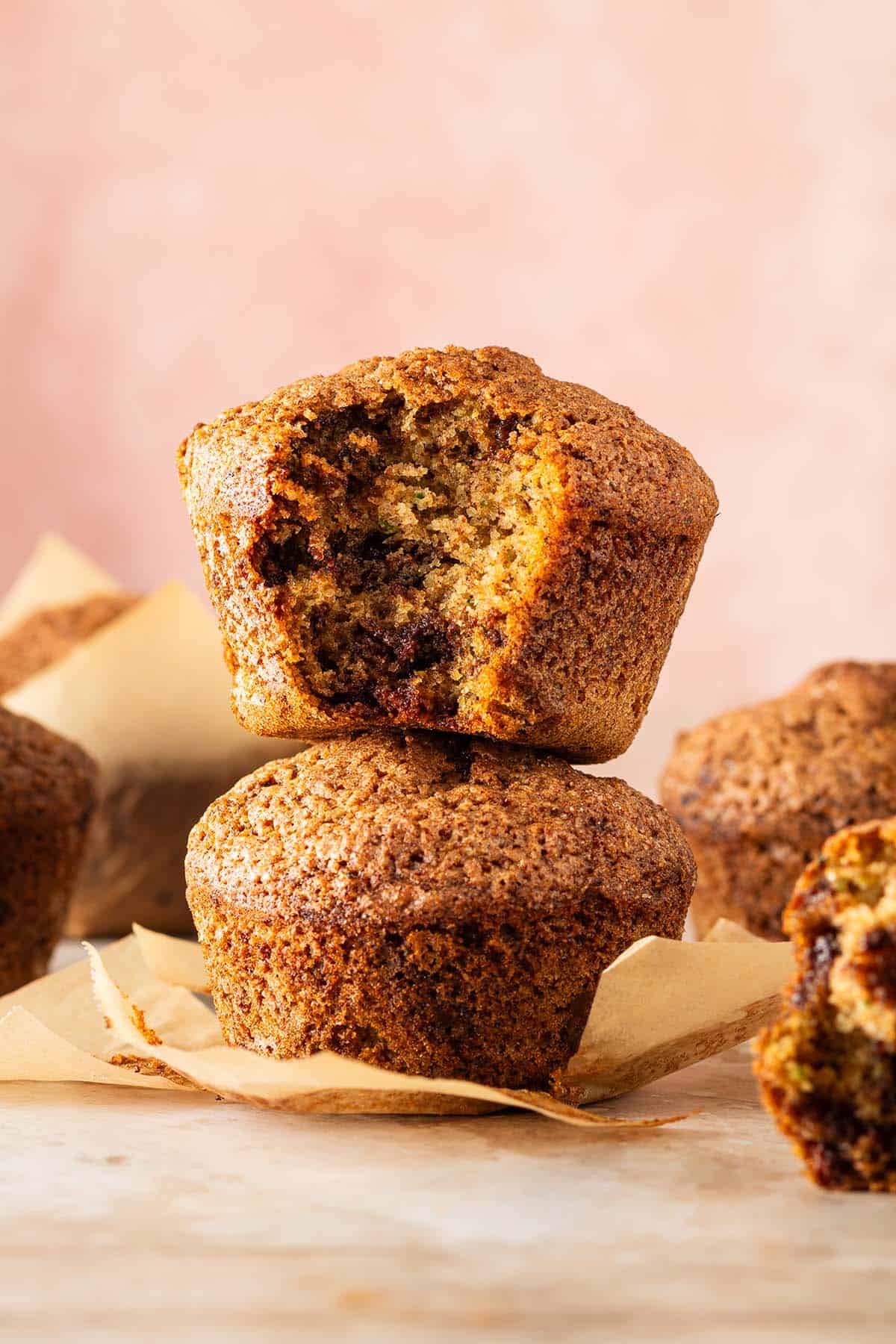 Zucchini Muffins mit saftiger Krume und geschmolzenen Schokostückchen, zwei davon aufeinander gestapelt, ein Muffin angebissen.