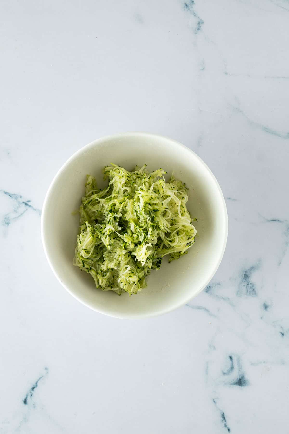 Fein geriebene Zucchini in einer Schüssel als Zutat für saftige Zucchini Muffins.