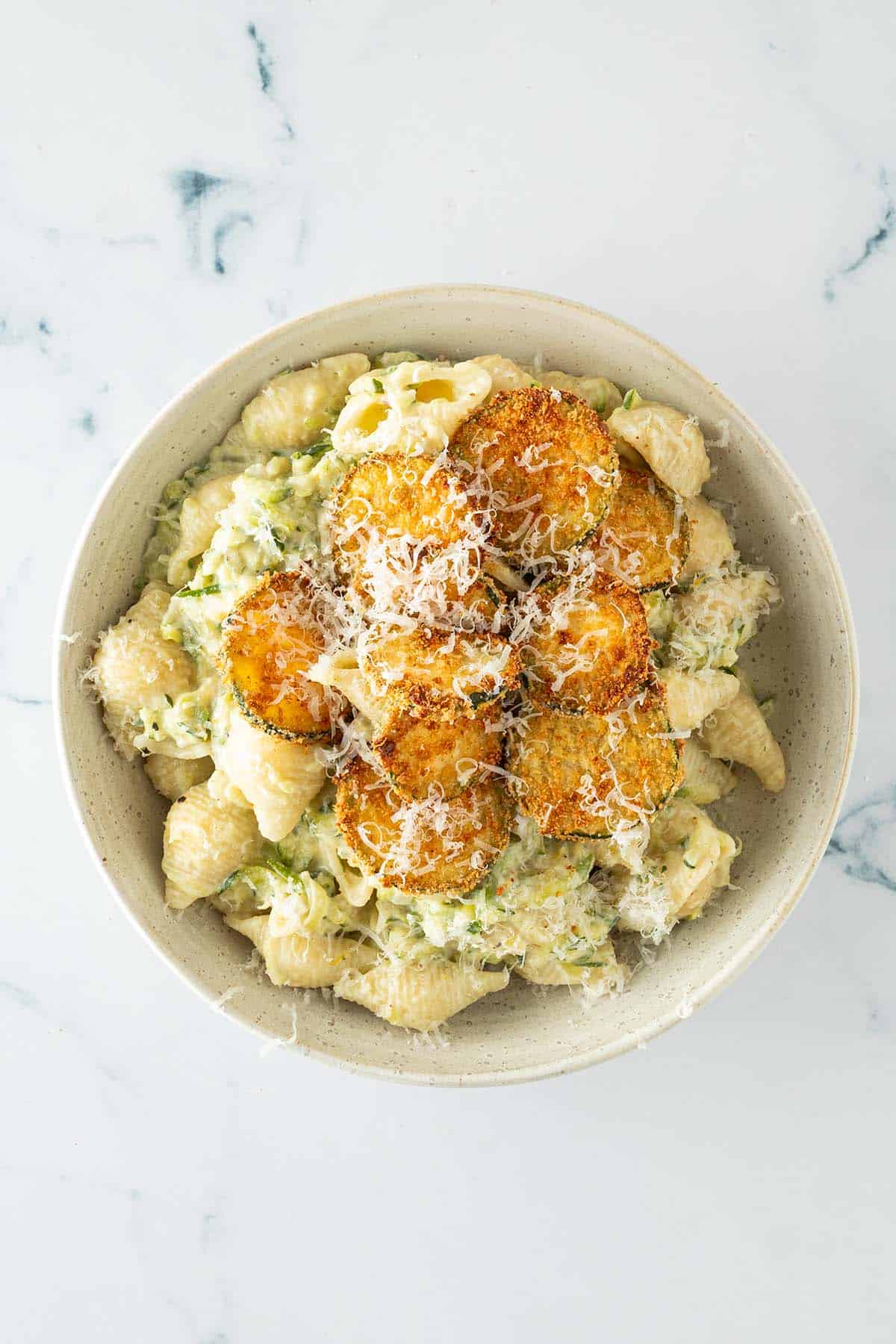 Cremige Zucchini Pasta serviert in einem Teller mit den knusprigen Zucchini-Chips und frisch geriebenem Parmesan als Topping.