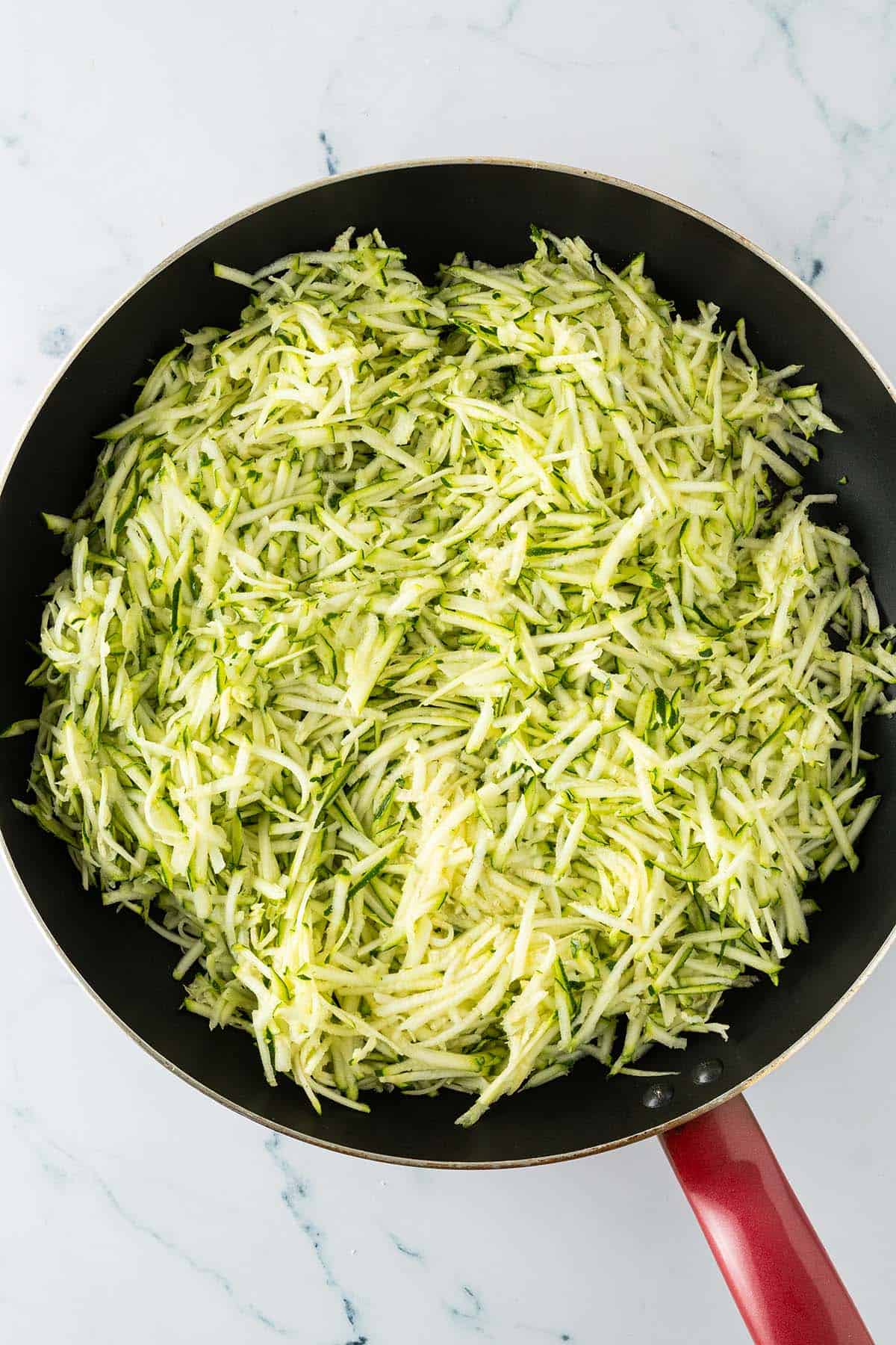 Grob geraspelte Zucchini in einer Pfanne als Basis für die Zucchini-Sauce.