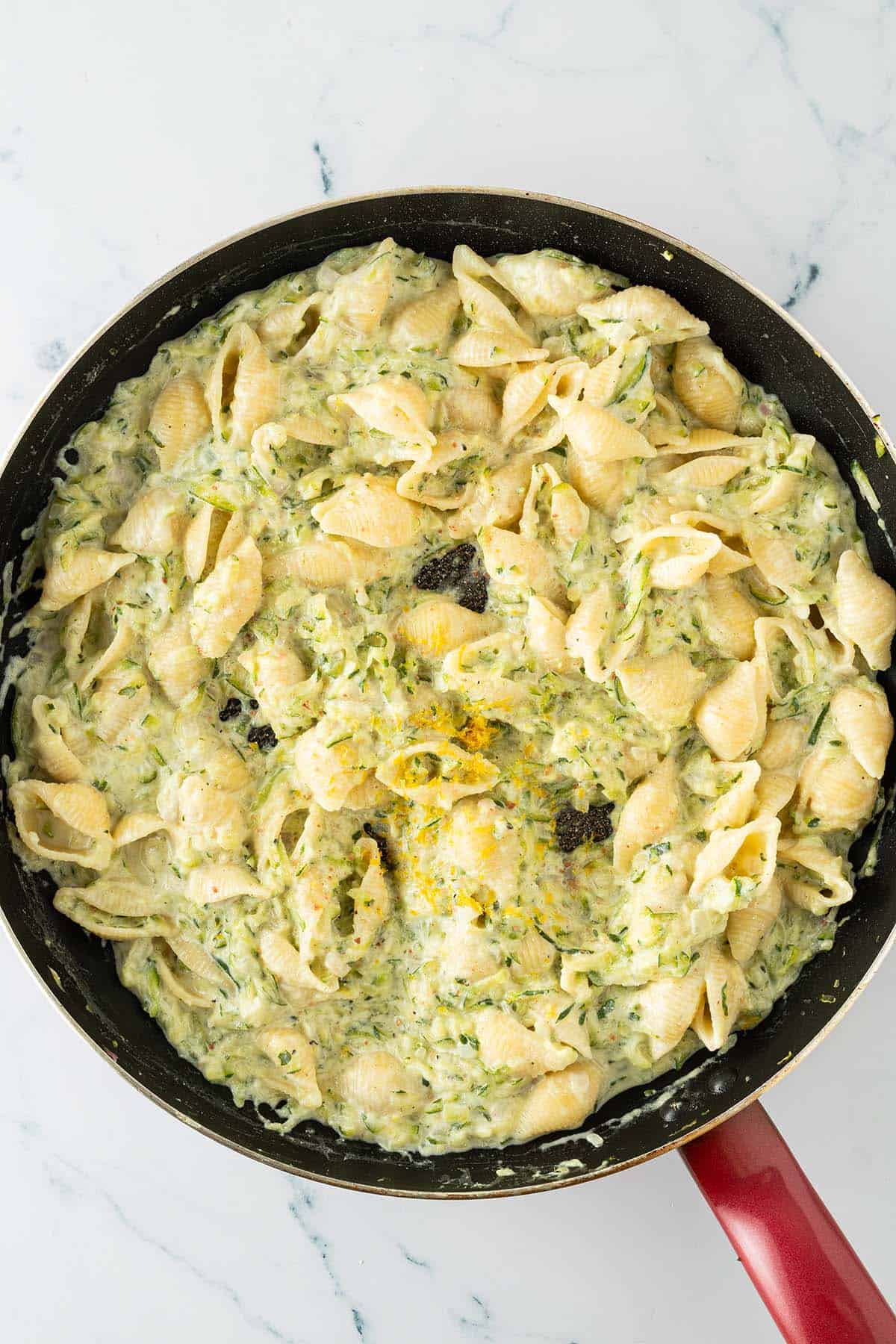 Eine große Pfanne mit Pasta in cremiger Zucchini-Ricotta-Sauce mit Zitronenabrieb.