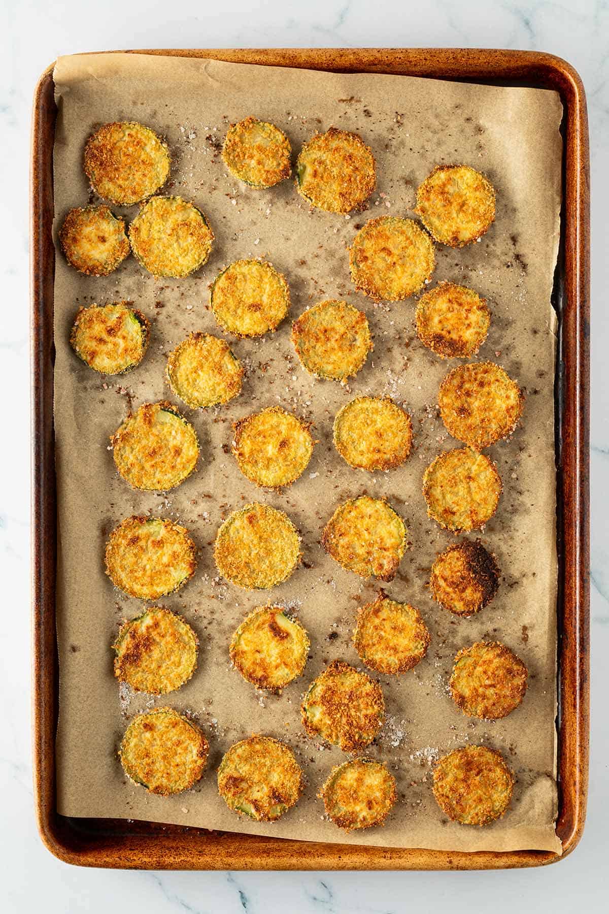 Knusprige, goldbraun gebackene Zucchini-Chips aus dem Ofen auf einem Backblech.
